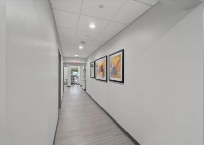 White corridor at Troy Oral Surgery in Troy, Michigan, with three framed abstract prints and a view through to a recovery room with a window