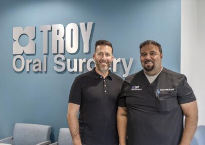 Remy Isdaner of Mirlo Real Estate Partners with Dr. Robert John in scrubs in front of the Troy Oral Surgery logo wall in Troy, Michigan