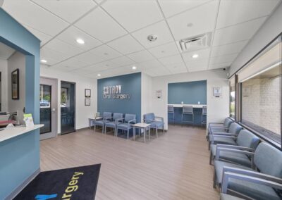 Beautiful, new waiting room at Troy Oral Surgery in Troy, Michigan, seen from the check-in window, with blue chairs along the windows, a counter with stools and the logo wall